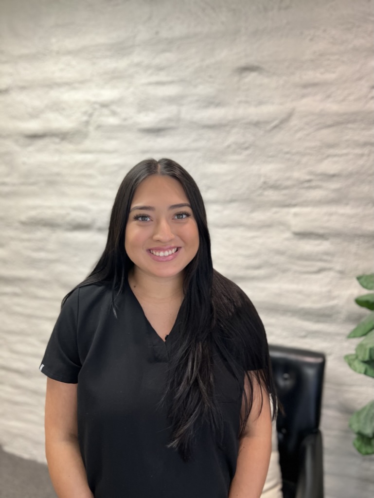 170EE358-27FD-44FF-BD16-6ADE34F4323A_1_105_c woman by chair and plant in black scrubs